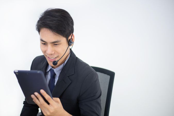 Asian man working at service desk talking on phone in a call center with tablet