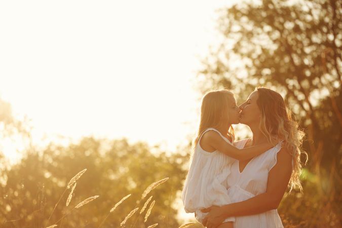Woman embracing little girl in marsh at sunset