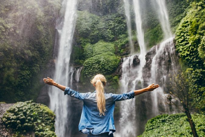 Female tourist with her arms outstretched looking at waterfall