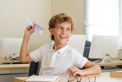 Delighted schoolboy playing with paper airplane in classroom