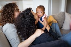 Moms on sofa kissing new baby