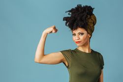 Studio shoot of confident Black woman smiling flexing her bicep