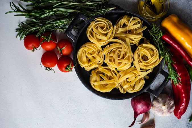 Top view of raw Fettuccine pasta in pan surrounded by fresh vegetables