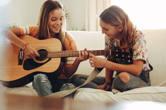 Two smiling teenage girls learning to play guitar at home