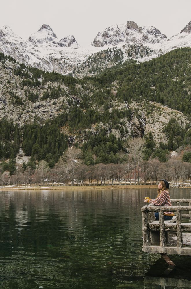 Woman on seat near wonderful lake between hills in snow and cloudy sky