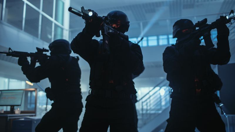 Masked Squad of Armed SWAT Police Officers Stand in Dark Seized Office Building with Desks and Computers.