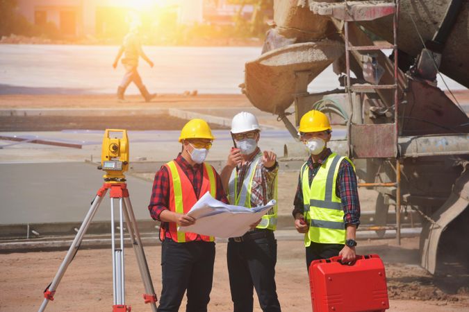 Three men wearing bump caps and facemask talking at the construction site
