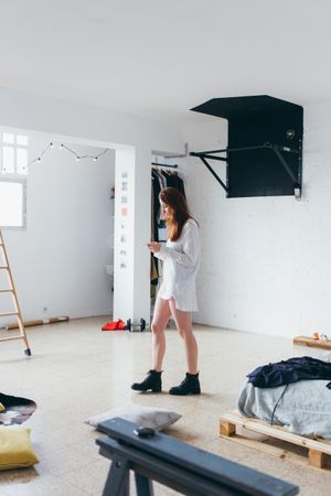 Woman looks down at phone in her bright apartment