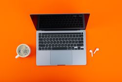 Looking down at laptop on orange desk with mug of coffee or tea and ear buds