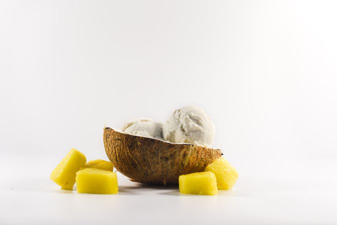 Side view of coconut shell with scoop of ice cream and pineapple fruit chunks