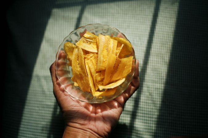 Hand holding dried banana slices in bowl in morning light