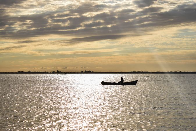 Silhouette of person riding on boat during sunset under cloudy sky