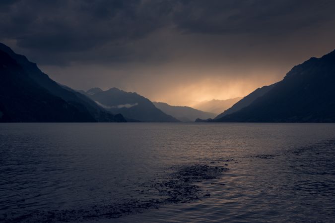 Gray water of lake in dark mountains under cloudy sky