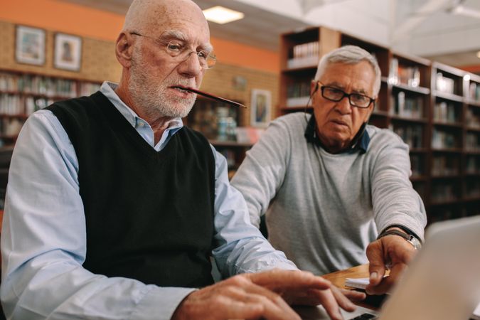 Two older men sitting in classroom and working together on a laptop computer