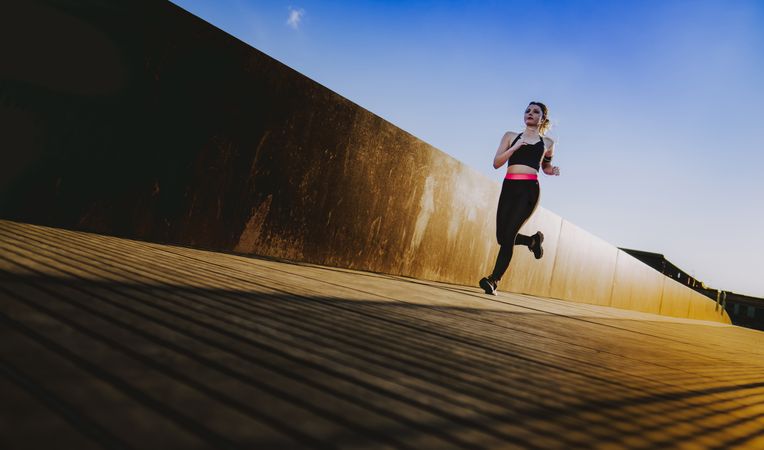Woman running on walkway in sunny day with blue sky