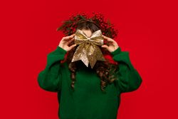Young girl playfully hiding face behind large golden glittery bow.