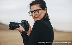 Portrait of photographer looking over her shoulder holding dslr 499x64