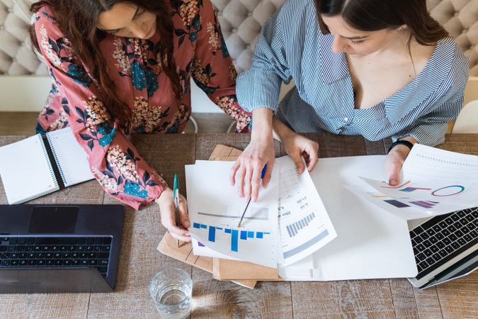 Crop focused female colleagues analyzing charts together in office