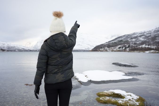 Anonymous person on pond shore against highland in winter