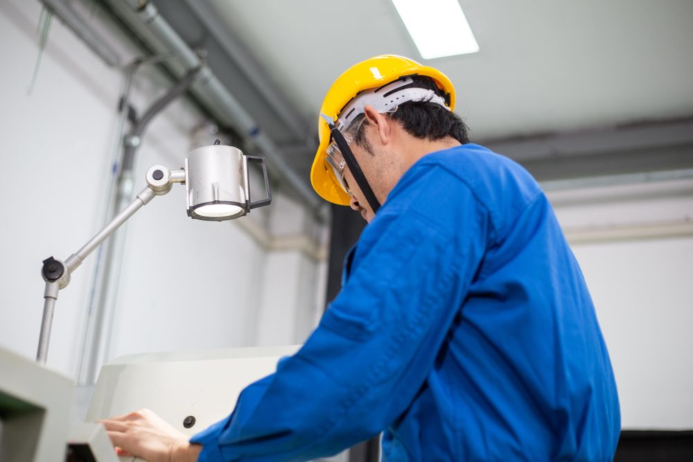 Asian male in blue jumpsuit and yellow hard hat working with machinery
