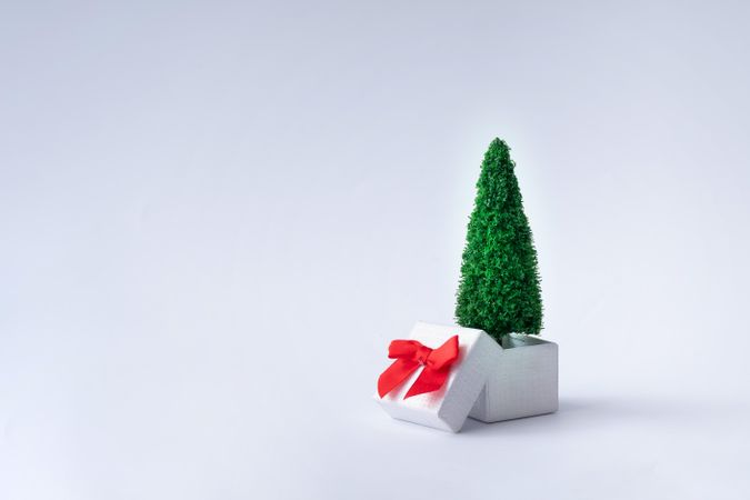 Christmas tree coming out of gift box with red bow on light background