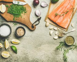 Salted salmon fillet with fresh herbs, limes, onions, bread board, copy space