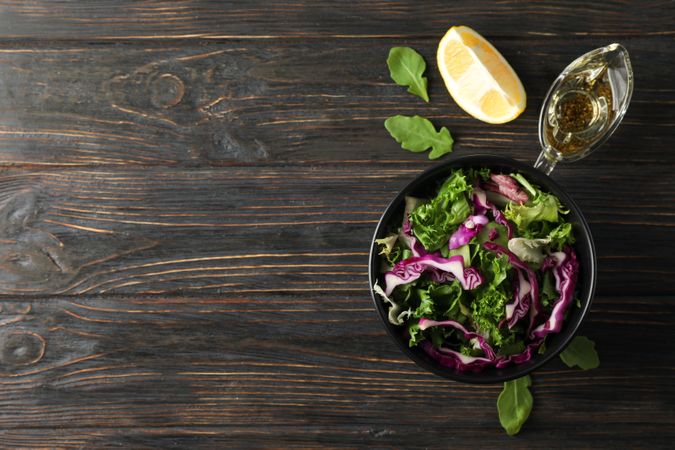 Black bowl with salad and ingredients on wooden background, top view