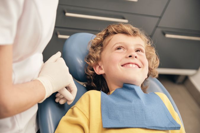 Joyful boy looking at unrecognizable dentist