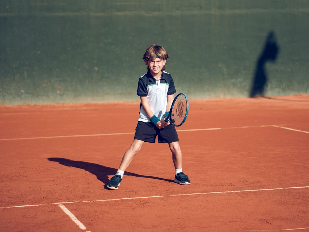 Happy child smiling while practicing tennis on clay court