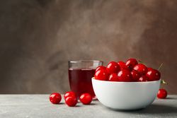 Bowl with red cherry and glass of juice on gray table, space for text