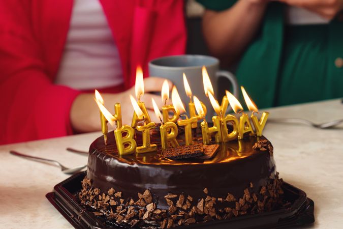 Birthday cake with golden candles burning, surrounded by chocolate pieces.