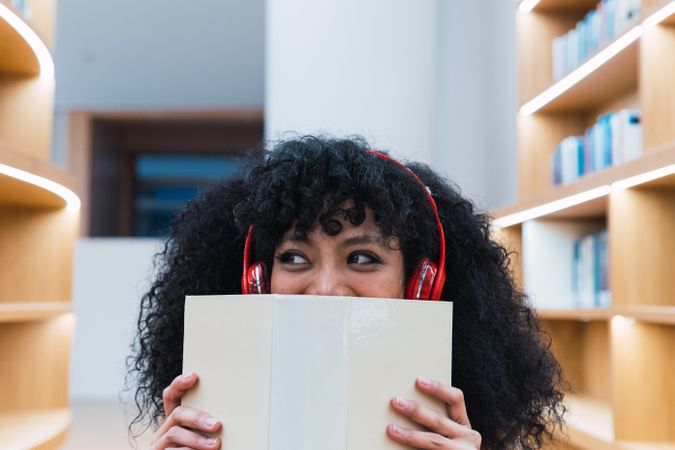 Positive Black woman in headphones with opened book in library