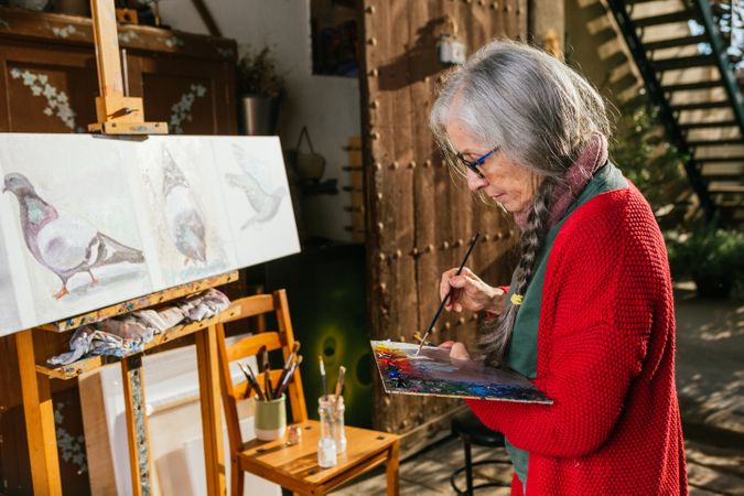 Older woman painting on canvas in garden