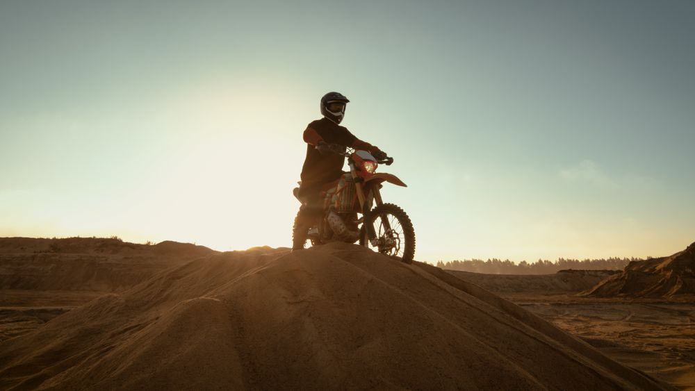Professional Motocross Rider on FMX Motorcycle Stands on the Sand Dune and Overlooks Whole Extreme Off-Road Terrain that He Gonna Ride Today.