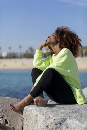 Smiling female in green shirt sitting on rocks near coast