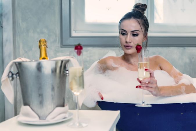 Dreamy woman in bathtub drinking champagne