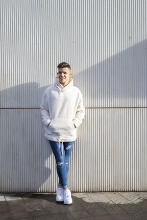 Portrait of young adult with hands in pocket standing in front of wall outside