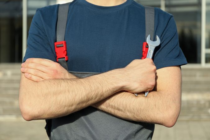 Man in overalls holding a wrench with folded arms. Car inspection
