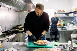 Male chef in gloves dressing assorted food in kitchen