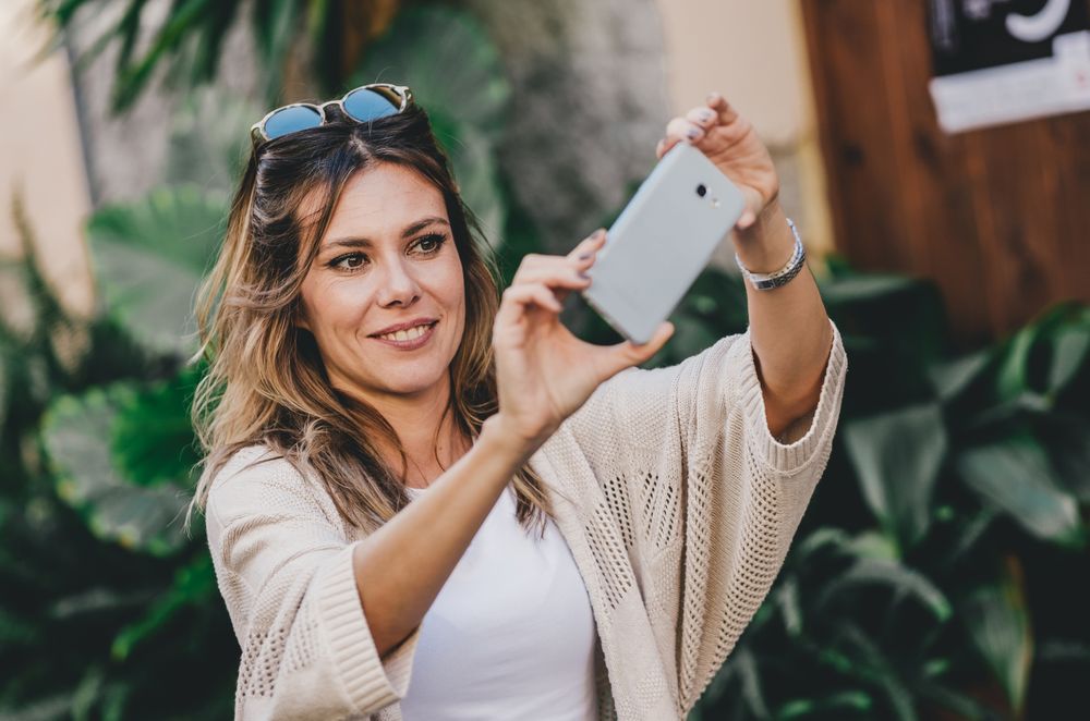 Smiling woman taking selfie in street city full of plants
