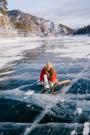 Woman sitting on frozen river and tying the shoelaces
