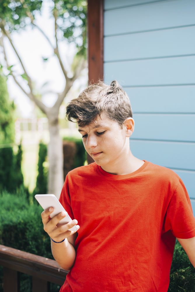 Serious teenage boy standing outside wearing red t-shirt using phone