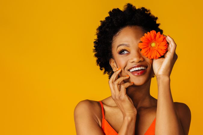 Happy Black woman holding a flower over her eye with her hand to her chin