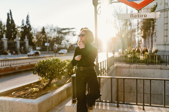 Stylish woman lighting cigarette near metro station