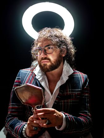 Serious man with glowing fake nimbus holding mirror and looking away