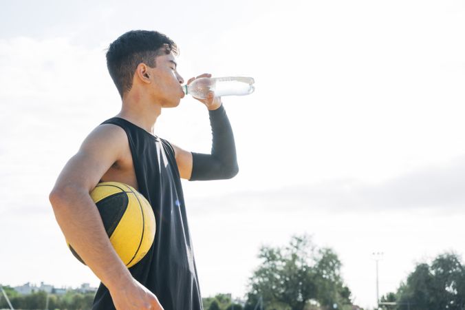 Young man playing on yellow basketball court outdoor drinking water