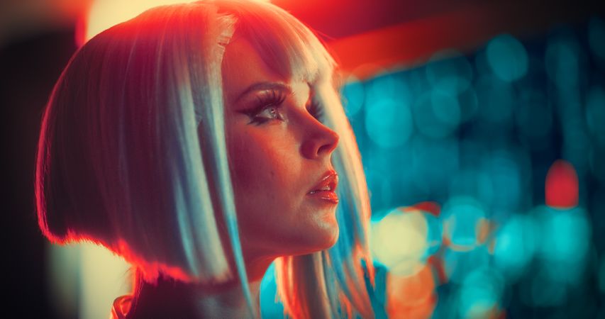 Cinematic Close Up Portrait of a Young Cosplay Model Wearing Futuristic Clothes, Striking Makeup and a Short Blue Wig, Female Enjoying a Beautiful Night Life Scenery in a Neon High Tech City