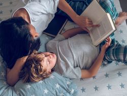 Mother and preteen son lying on bed and reading