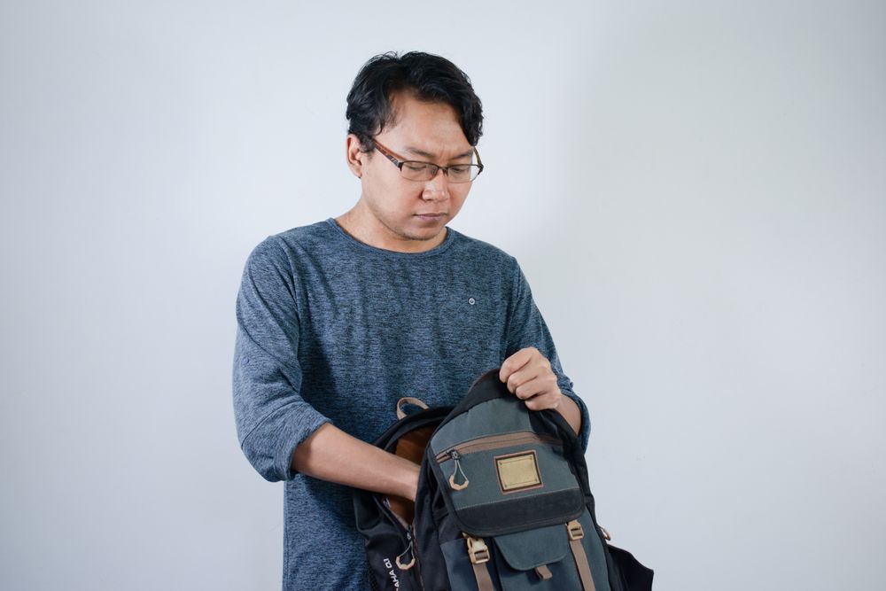 Asian student male looking for book in bag with happy gesture