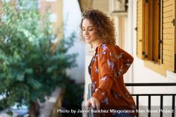 Happy young woman in casual wear with curly hair standing on balcony 4AzgME